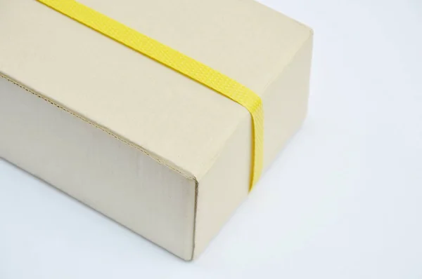 Wenkbrauw harde papier doos verpakt door gele kunststof band op witte achtergrond — Stockfoto