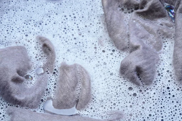 Camisa gris remojo en polvo detergente disolución de agua en lavabo de plástico negro — Foto de Stock