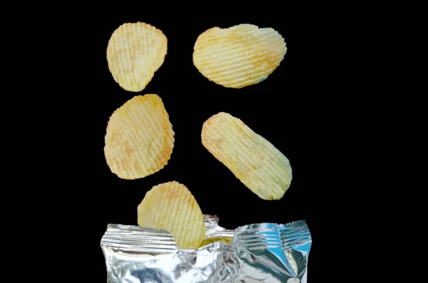 Kartoffelsplitter Fallen Auf Alufolienverpackung Auf Schwarzem Hintergrund — Stockfoto