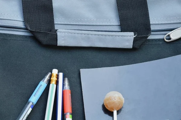 Lápiz pluma y libro con piruleta en maletín de tela negro —  Fotos de Stock