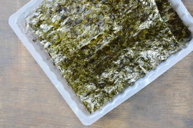  ahşap arka plan üzerinde plastik tepsi içinde yemek pişirmek için çiğ deniz yosunu