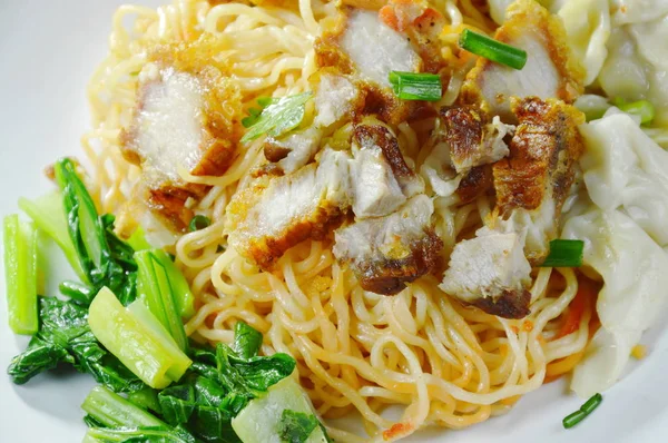 dry Chinese egg noodles topping crispy pork and dumpling on plate