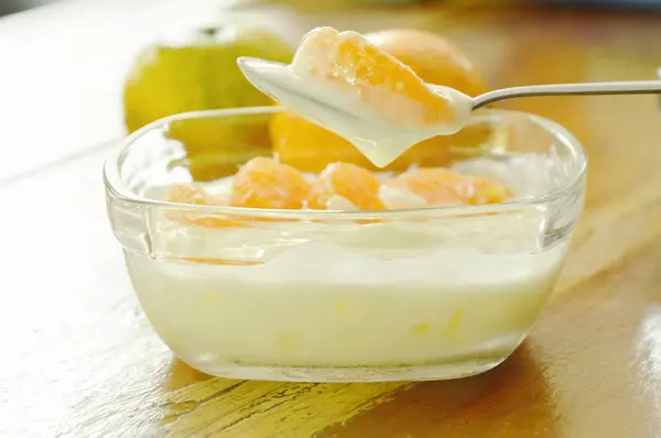 โยเกิร์ตท็อปปิ้งส้มบนช้อนในถ้วยแก้ว — ภาพถ่ายสต็อก