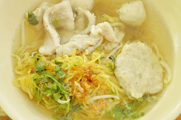 Fideos amarillos chinos cubriendo rebanada de cerdo y bola en sopa clara — Foto de Stock