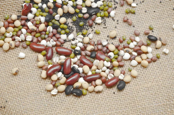 Varietà grezza di fagioli e piante di cereali che si diffondono sul sacco — Foto Stock