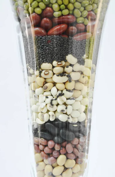 Varietà grezza di fagioli e cereali in vetro su fondo bianco — Foto Stock