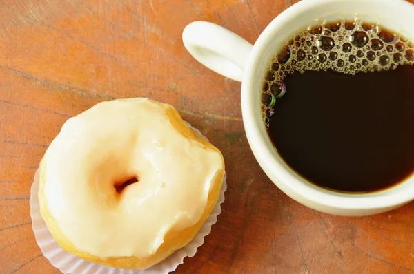 Пончики с белым кремом и черная чашка кофе на фоне деревянной доски — стоковое фото