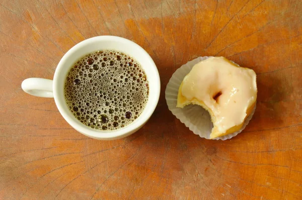 Ciambelle crema bianca mordere e tazza di caffè nero su sfondo bordo di legno — Foto Stock