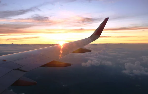 飛行機の翼と雲が夕日の窓枠を通って空に浮かんでいます — ストック写真