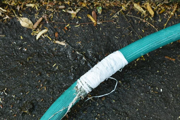 Grieta tubo de goma de riego verde reparación por rollo de cinta blanca con hoja seca en el patio delantero suelo de jardín — Foto de Stock