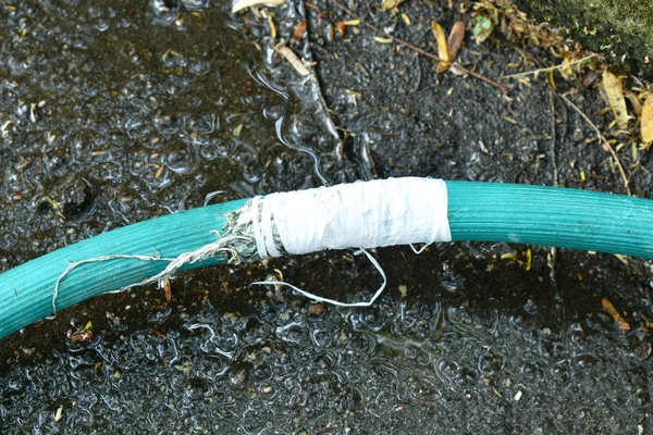 Grieta tubo de goma de riego verde reparación por rollo de cinta blanca con hoja seca en el patio delantero suelo de jardín — Foto de Stock