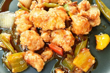  Kızarmış kızarmış tavuk ve dilimlenmiş dolmalık biber ve tatlı soslu siyah tabak.