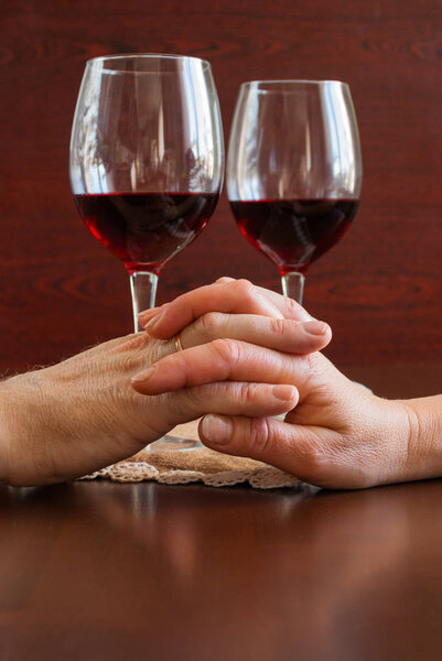 Two glasses of wine on a wooden table.  Hands.