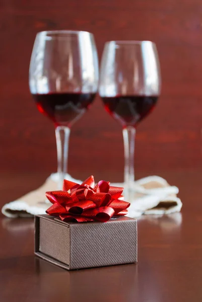 Zwei Gläser Wein auf einem Holztisch. braune Schachtel mit Schleife. — Stockfoto