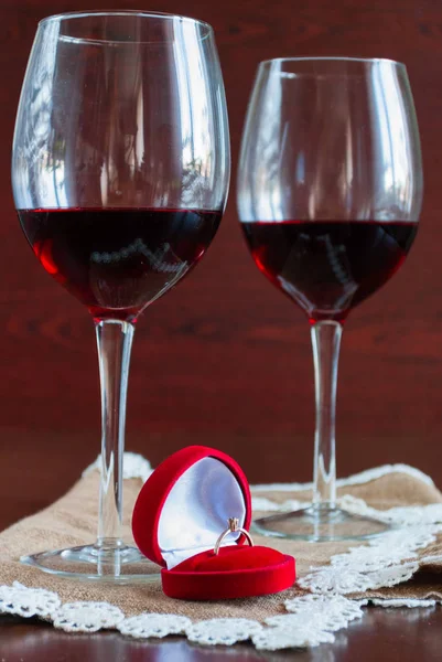 Dos copas de vino sobre una mesa de madera. Caja roja con anillo de compromiso — Foto de Stock