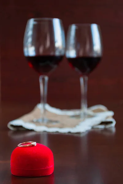 Dos copas de vino sobre una mesa de madera. Caja roja con anillo de compromiso — Foto de Stock