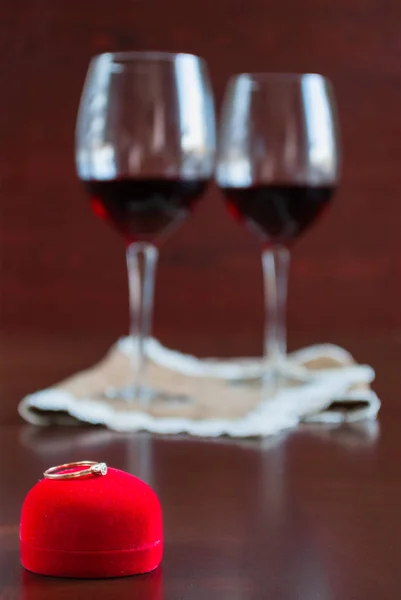 Dos copas de vino sobre una mesa de madera. Caja roja con anillo de compromiso — Foto de Stock