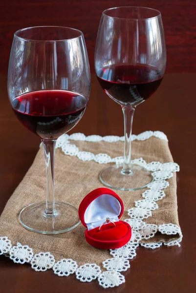 Dos copas de vino sobre una mesa de madera. Caja roja con anillo de compromiso — Foto de Stock