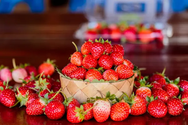 Ripe strawberries with leaves in wicker basket on wooden table o — Stock Photo, Image