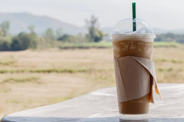 Iced coffee with straw in plastic cup on a wooden table in summe