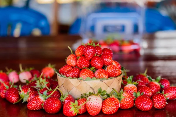 Ripe strawberries with leaves in wicker basket on wooden table o — Stock Photo, Image