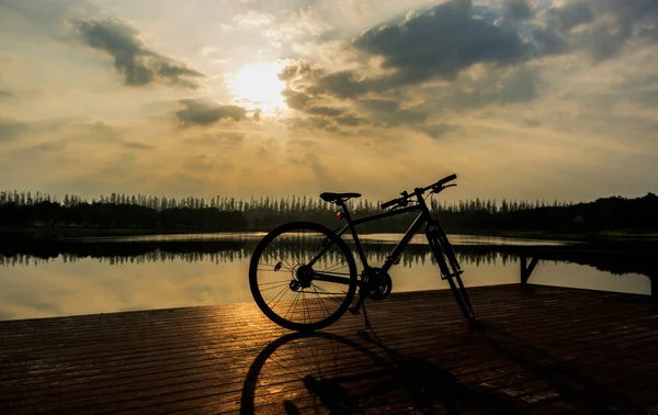 Silueta de bicicleta cerca del lago y puesta del sol en el cielo hermoso — Foto de Stock