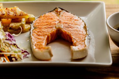 Ahşap bir masa üzerinde beyaz bir tabak içinde somon steak.