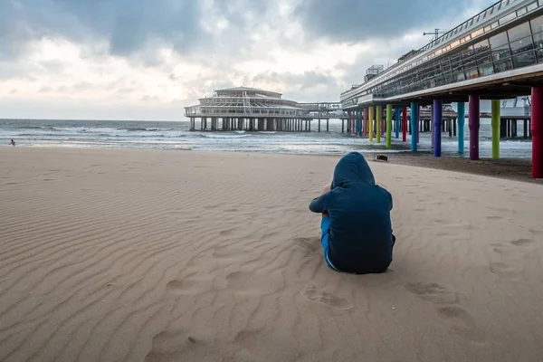 Lány visel egy kapucnis pulcsit, közelében a mólón, a strandon a suns ült — Stock Fotó