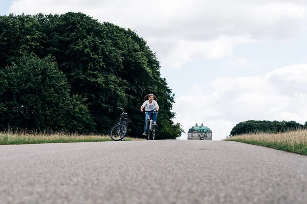 Hübsche junge Frau radelt auf einer Landstraße im Park — Stockfoto