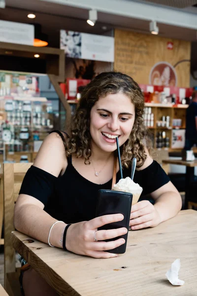 Happy girl laughing drinking ice coffe and texting on her phone — Stock Photo, Image