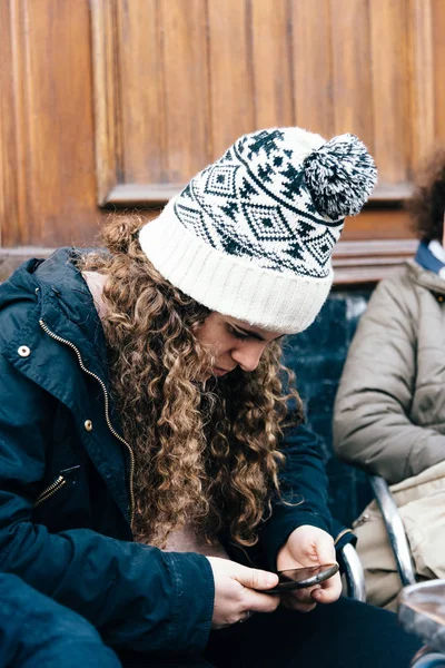 Teenage girl in knit hat texting with cell phone