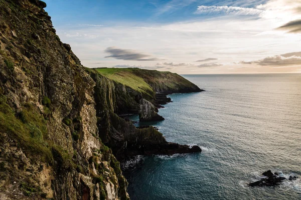 Vista panorâmica de falésias na costa irlandesa com colinas verdes ao pôr-do-sol . — Fotografia de Stock