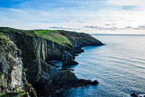 Vista panorâmica de falésias na costa irlandesa com colinas verdes ao pôr-do-sol . — Fotografia de Stock