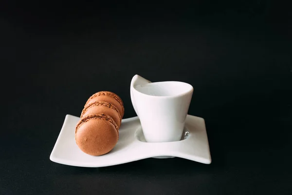 Set of cup of coffee and macarons against black background — Stock Photo, Image