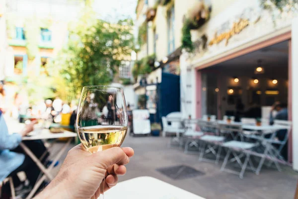 Man holds a glass of white wine in a trendy shopping area sitting on a terrace — Stock Photo, Image