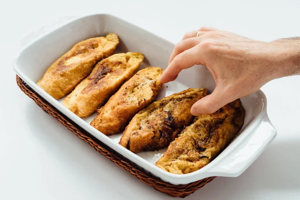 Male hand taking torrijas, typical Spanish sweet fried toasts of sliced bread soaked in eggs and milk on tray isolated. — Stock Photo, Image