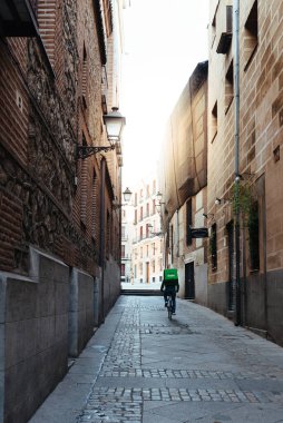 Uber Eats sürücüsü eski Madrid 'de bir ara sokakta bisiklet sürüyor