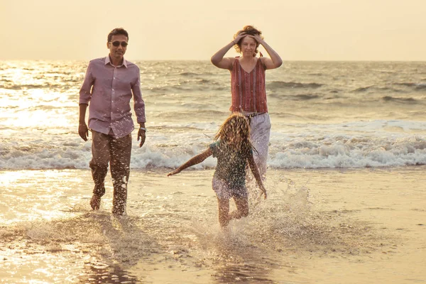 Familia de raza mixta jugando con un niño en el mar al atardecer — Foto de Stock