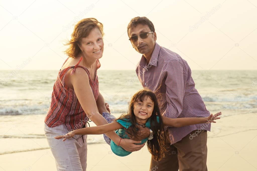 Mixed race family playing with child on sea at sunset