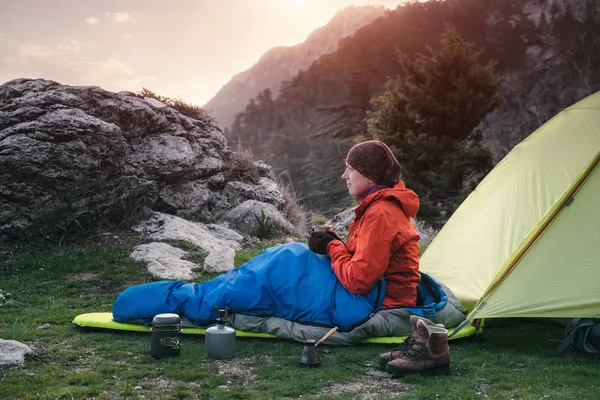 Женщина-путешественница в спальном мешке рядом с палаткой в горах — стоковое фото