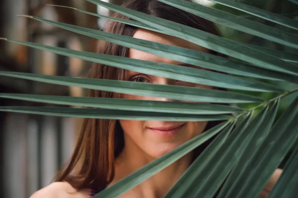Misterioasă tânără caucaziană care se ascunde în spatele frunzei de palmier — Fotografie, imagine de stoc