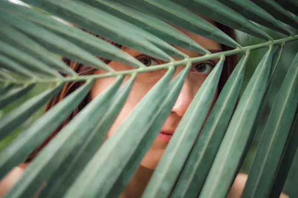 Крупный план молодой женщины, смотрящей сквозь пальмовый лист — стоковое фото
