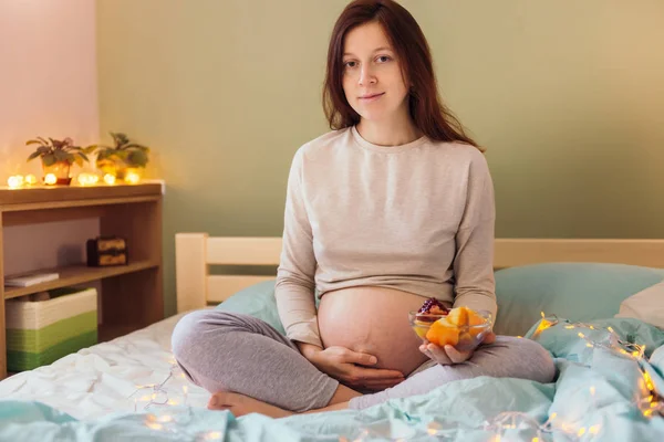 Mujer embarazada joven natural en la cama con frutas — Foto de Stock