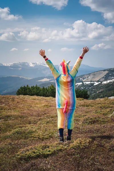 Funny travel, female hiker in a unicorn suit celebrating success, standing on top of the mountain overlooking Carpathian landscape on a Spring day. Wanderlust concept.