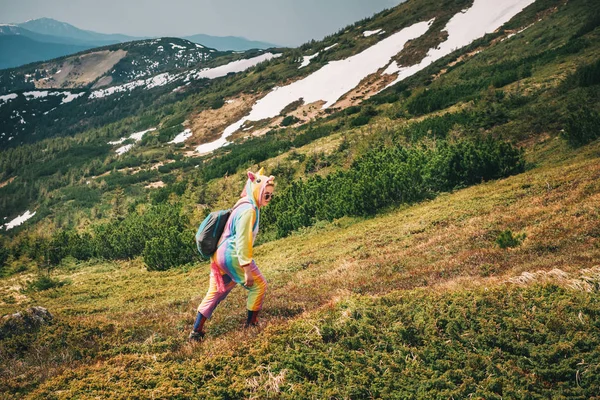 Funny backpacker in a unicorn costume hiking in the mountains. Travel and freedom concept