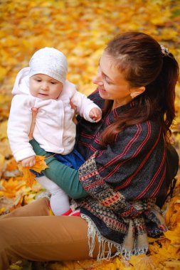 Anne dizli ve sonbahar ormanında oynayan küçük bir kız.