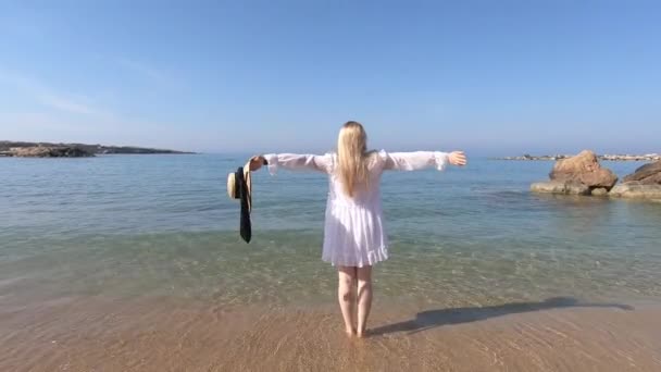 白い服を着た美しいブロンドの女性が珊瑚湾のビーチを歩いている キプロスへの旅行 自由夏のコンセプト — ストック動画