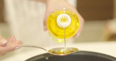 Kadın mutfaktaki tabağa zeytinyağı ekliyor.