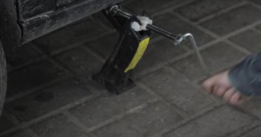 Yakışıklı sürücü unscrewing araba tekerlek üzerinde yol kenarı düz lastik değiştirmek için yol kenarında Pnömatik anahtarı tarafından. Adam araba tekerlek lastiği yolculuk sırasında değiştirdikten sonra anahtar ile uygun rahat kıyafetler.
