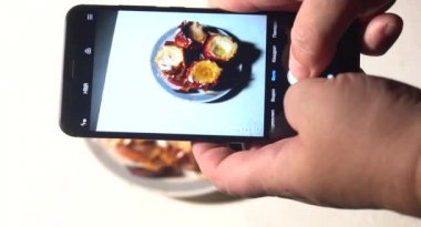 Restoranda telefonla öğle yemeği fotoğrafı çeken genç bir adam. Genç bir adam akıllı telefondan kek fotoğrafı çekiyor, cep kamerasıyla yemek çekiyor..